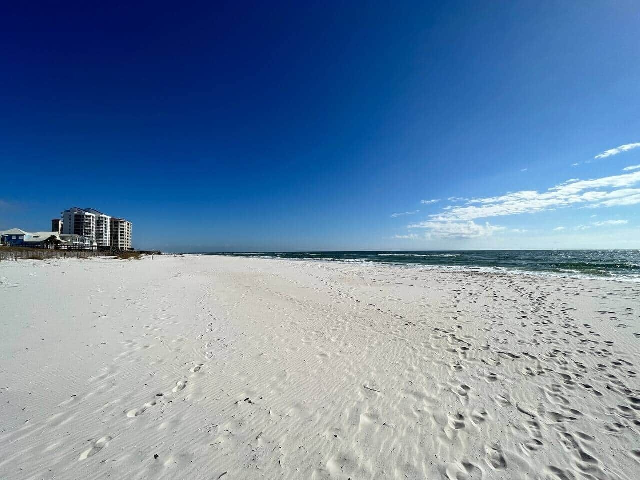 A beach with footprints leading to a building with multiple floors.