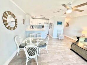 Uma cozinha moderna com armários brancos, micro-ondas e geladeira. Há uma área de refeições com cadeiras e mesa brancas.