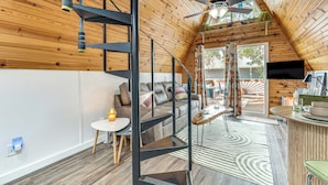 Une pièce de style loft avec un plafond en bois, un escalier, un canapé, un coin repas et un téléviseur.