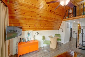 Een houten plafond met een ventilator, een televisie, een tafel met stoelen, en een keuken met een fornuis.