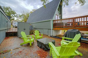Eine Terrasse mit grünen Adirondack-Stühlen, einem überdachten Tisch und einem Grill.