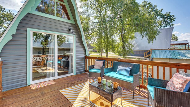 Une terrasse en bois avec des meubles en osier, une porte d’entrée en verre et une vue sur les environs.