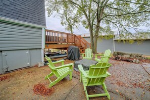 Een terras met groene Adirondack stoelen, een overdekte barbecue en een houten terras dat naar een huis leidt.