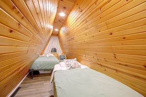 Una habitación estrecha con paneles de madera, dos camas, un ventanal y una lámpara en el techo.