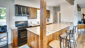 A modern kitchen with wooden cabinets, a large island with bar stools, a built-in oven, and a microwave. - Fire Pit + Private Dock: Ozarks Family Escape! (Camdenton)