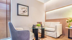 Une pièce moderne avec une table en verre, un fauteuil gris, un canapé et une œuvre d’art encadrée accrochée au mur.