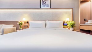 Une chambre d’hôtel moderne, dotée d’un grand lit, de tables de chevet avec des lampes, d’une horloge numérique et d’une œuvre d’art encadrée au mur.