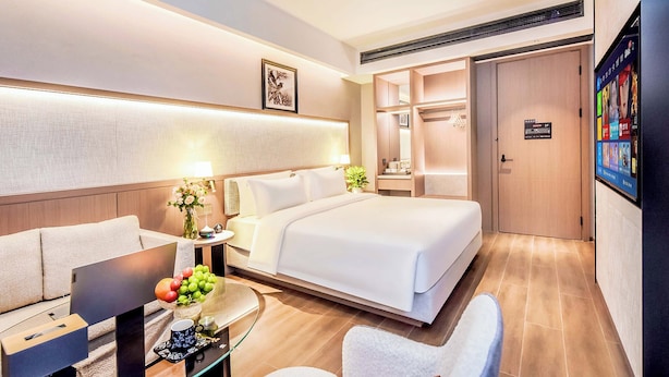 Une chambre d’hôtel moderne dotée d’un grand lit, d’un coin salon avec une table, d’une télévision et d’une armoire.