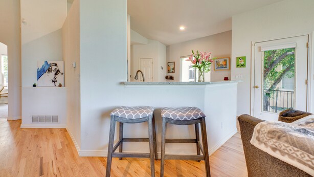 A modern kitchen with two stools, a white countertop, and a door leading to a balcony. - Pet-Friendly Longmont Home w/ McIntosh Lake Access (Longmont)