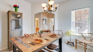 A dining area with a wooden table set for two, a chandelier, and a view of a brick wall through a window. - Pet-Friendly Longmont Home w/ McIntosh Lake Access (Longmont)
