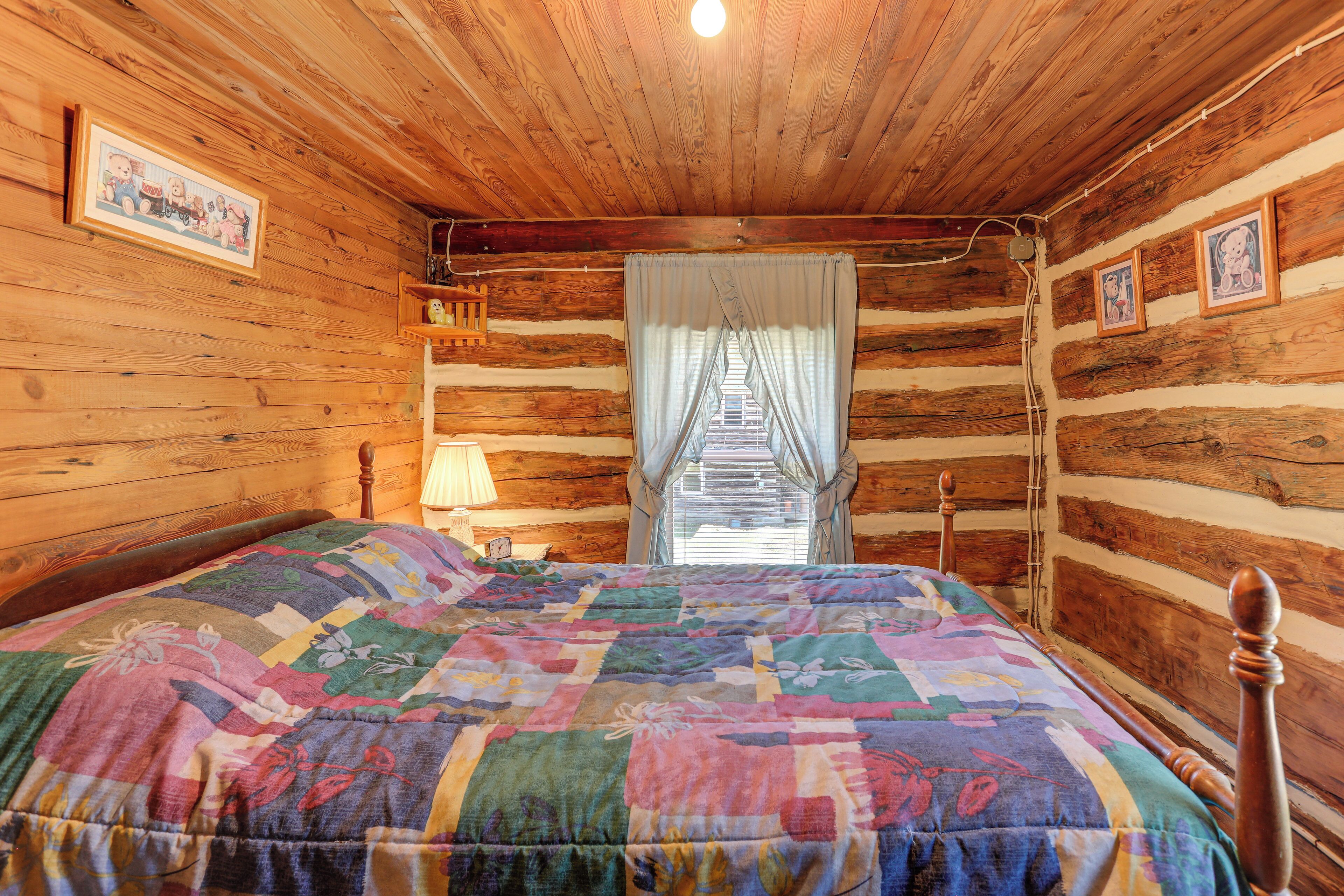 Une chambre dans un chalet en bois, avec un lit, une table de chevet, une lampe et une fenêtre avec des rideaux.