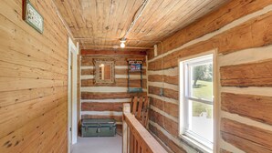 Ein Blockhaus-Interieur mit einer Holztreppe, einem Fenster mit Blick ins Grüne und einer an der Wand stehenden Leiter.