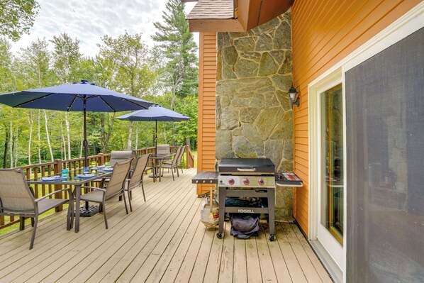 Una terraza al aire libre con una parrilla, mesa de comedor, sillas y sombrillas.
