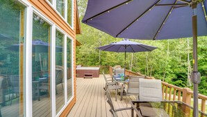 Una terraza de madera con mobiliario exterior, incluyendo sillas y una mesa, y dos grandes sombrillas que ofrecen sombra.
