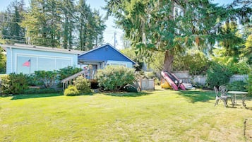 Una propiedad residencial con una casa azul, un porche cubierto y un patio trasero con un tobogán.