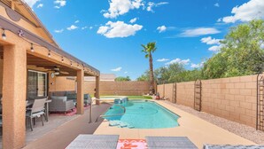 A backyard with a swimming pool, patio furniture, and a covered seating area.