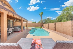 A backyard with a swimming pool, patio furniture, and a covered seating area.