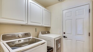 A laundry room with a Samsung washer and dryer, a trash can, and a white door.