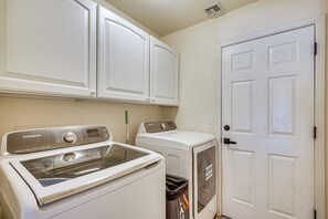 A laundry room with a Samsung washer and dryer, a trash can, and a white door.