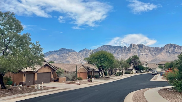 A residential street with houses, a clear sky, and mountains in the background.