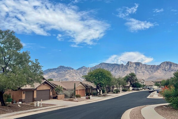 A residential street with houses, a clear sky, and mountains in the background.