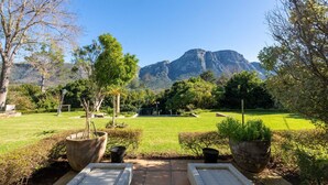 A patio with two white wicker lounge chairs, a well-maintained lawn, and a view of a mountain range.