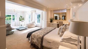 A spacious bedroom with a large bed, a sitting area with a sofa and coffee table, a bathroom with a mirror, and a view of greenery outside.