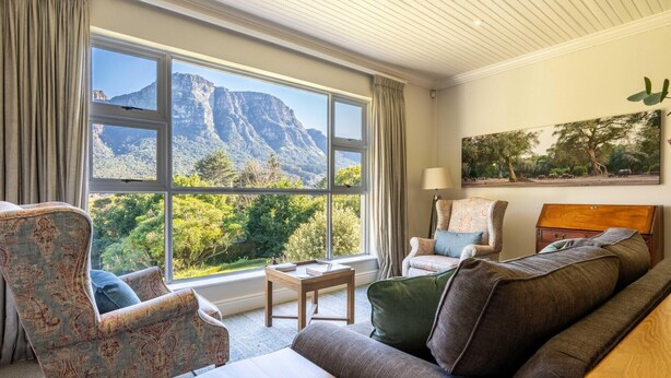 A room with a large window offering a mountain view, a sofa, a chair, and a small table.