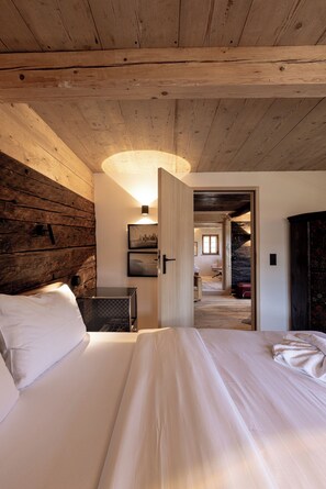 A bedroom with a wooden ceiling, a bed with white linens, a wall-mounted radiator, and a door leading to another room. - Four-bedroom vacation home, 200 m² (Reit im Winkl)