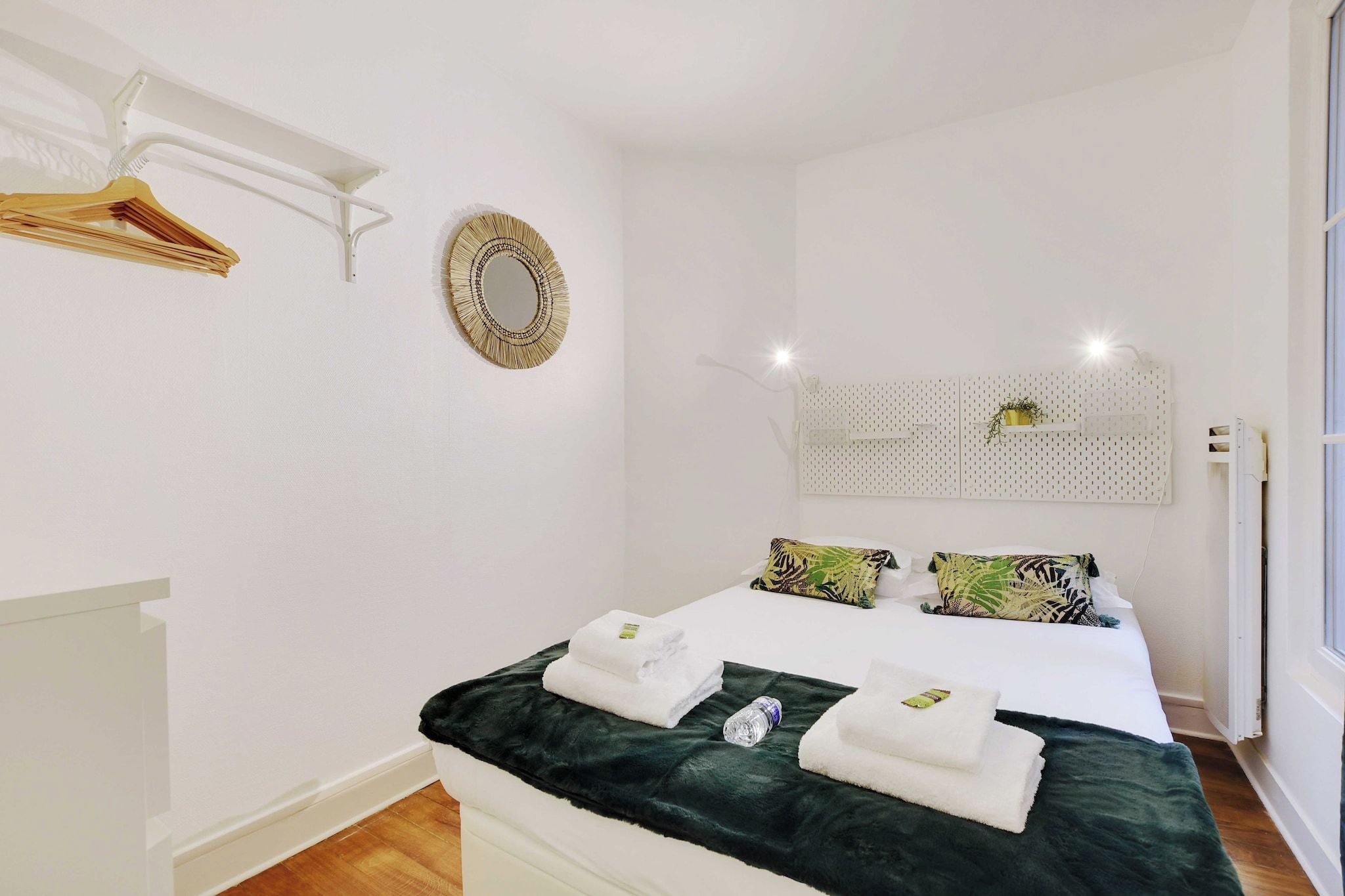 A neatly made bed with towels, a mirror, and a hanging rack.
