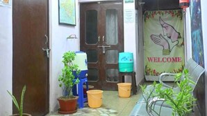 Un couloir étroit, doté d’un sol carrelé, de plantes en pot, d’une pancarte de bienvenue et d’une porte donnant sur une autre pièce.
