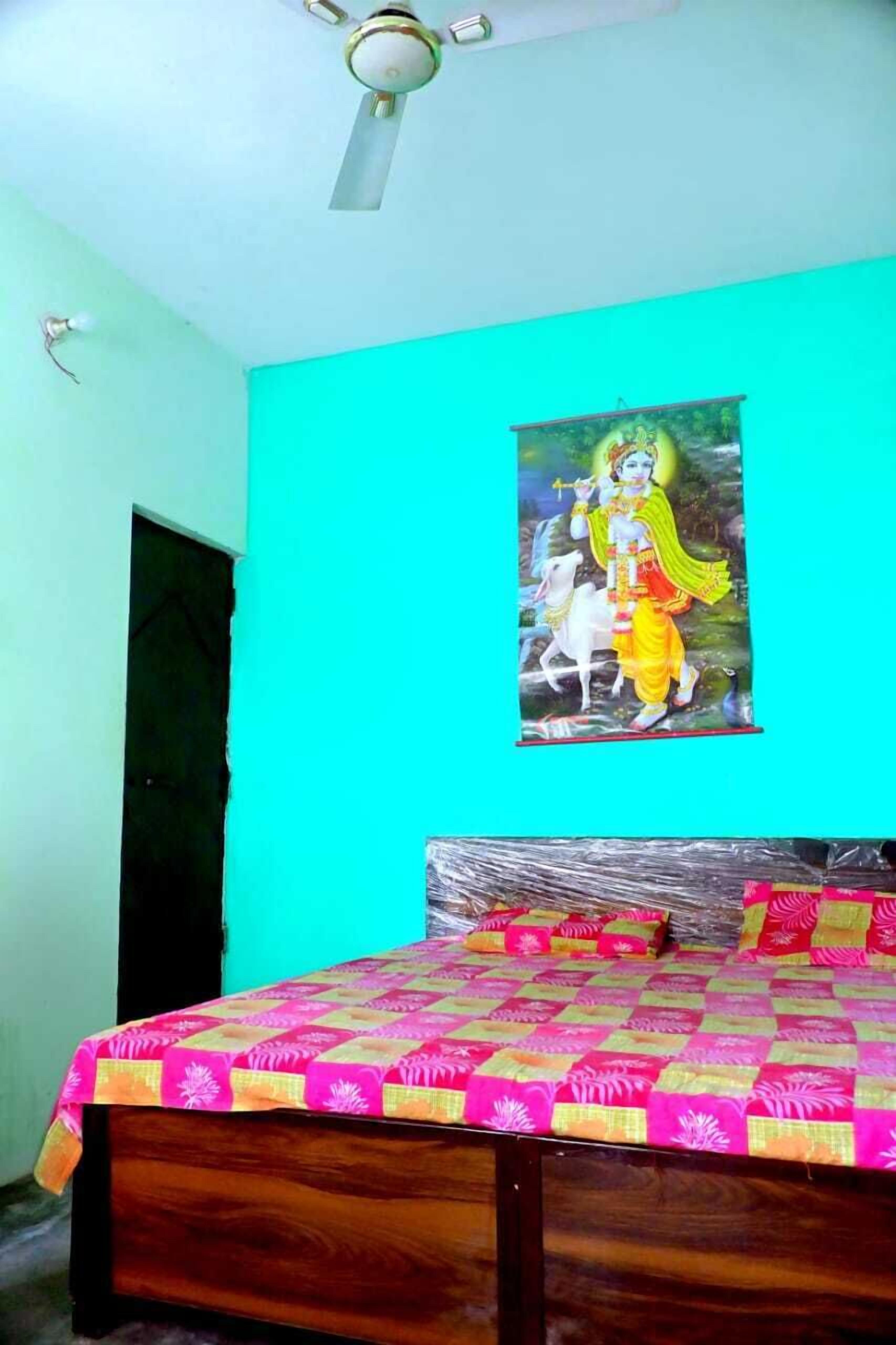 Ein Schlafzimmer mit einem Bett, das mit einer farbenfrohen Quilterdecke bezogen ist, einem Deckenventilator und einer Wand mit einem religiösen Poster.