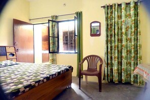 A bedroom with a bed, a chair, a window with curtains, and a mirror on the wall. - Maa Ganga Haveli Haridwar Homestay (Haridwar)