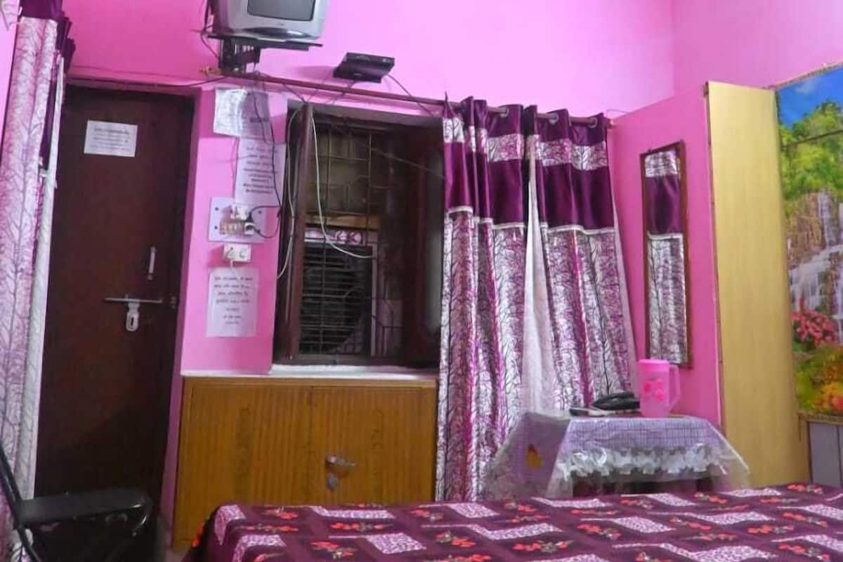 Ein Schlafzimmer mit einem Bett, einem Deckenventilator, einem Fernseher auf einem Regal und einem Fenster mit Vorhängen.