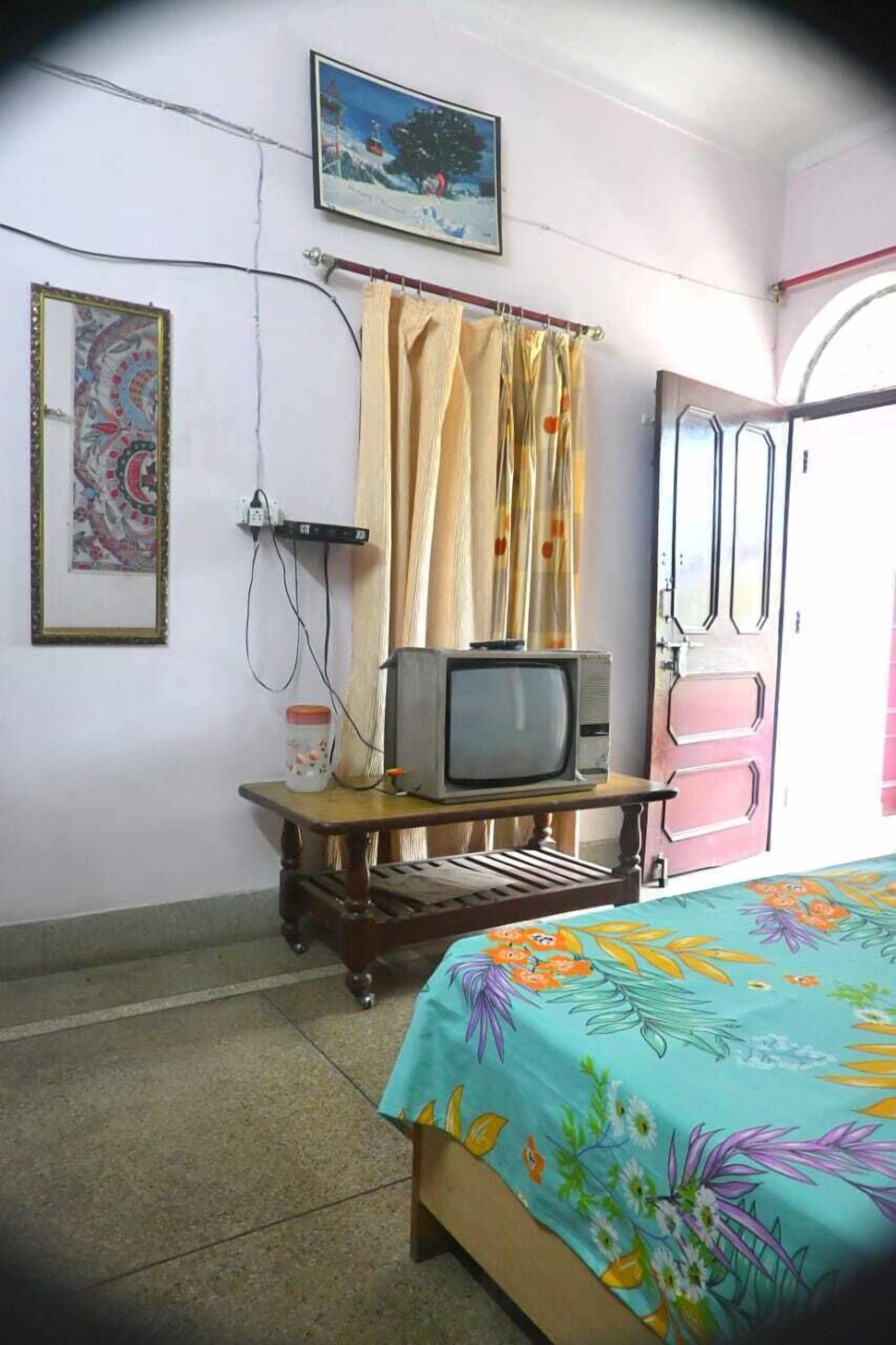 Un dormitorio con una cama, un televisor sobre un mueble de madera, una puerta y un cuadro en la pared.