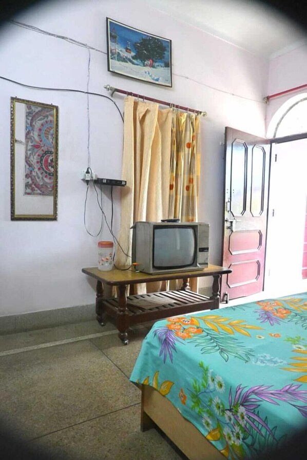 A bedroom with a bed, a television on a wooden stand, a door, and a wall with a painting.