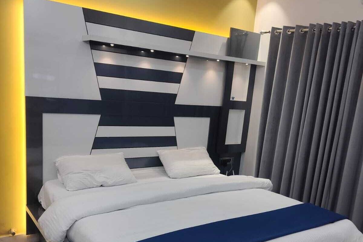 Une chambre à coucher moderne avec un grand lit, une tête de lit ornée de motifs géométriques et un rideau à la fenêtre.