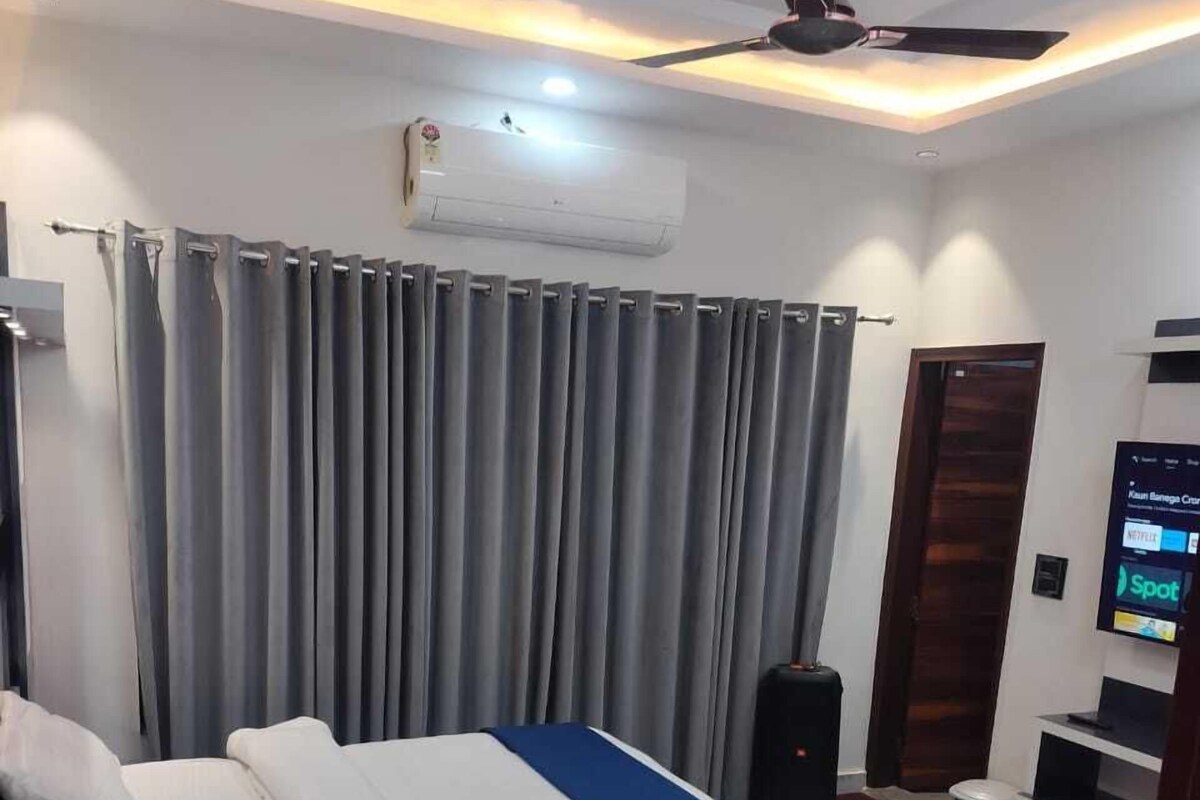 A modern hotel room with a large bed, a ceiling fan, an air conditioning unit, a television, and a digital screen displaying content.