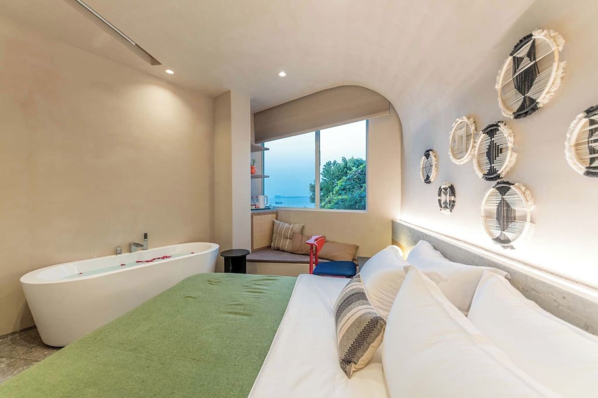 Une chambre d’hôtel moderne avec un grand lit, une baignoire et une fenêtre donnant sur la mer.
