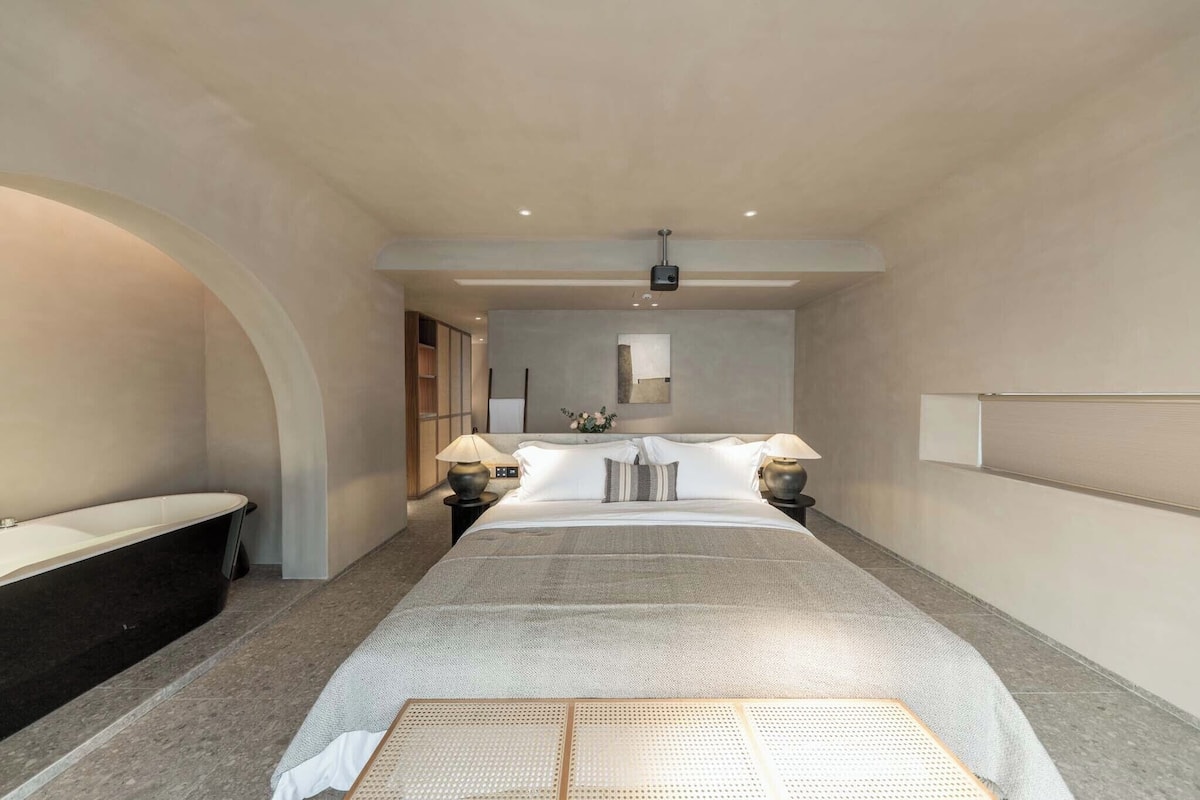 Une chambre d’hôtel moderne dotée d’un grand lit, d’une baignoire intégrée et d’un design minimaliste.