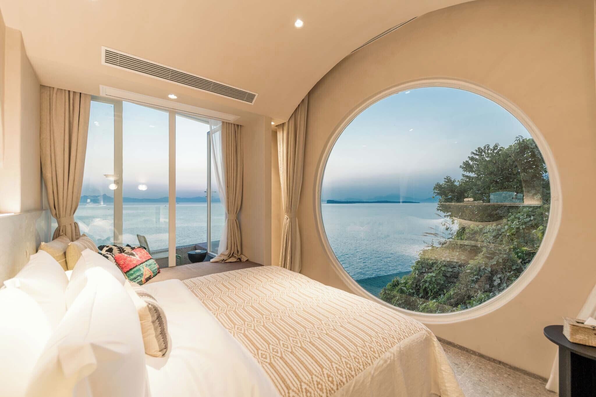 A bedroom with a large round window offering a view of the sea and cliffs.