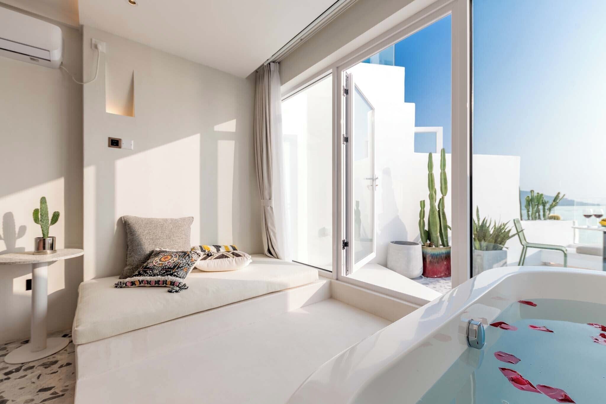 Une chambre moderne dotée d’une grande fenêtre, d’une baignoire blanche et d’un coin salon avec des coussins.