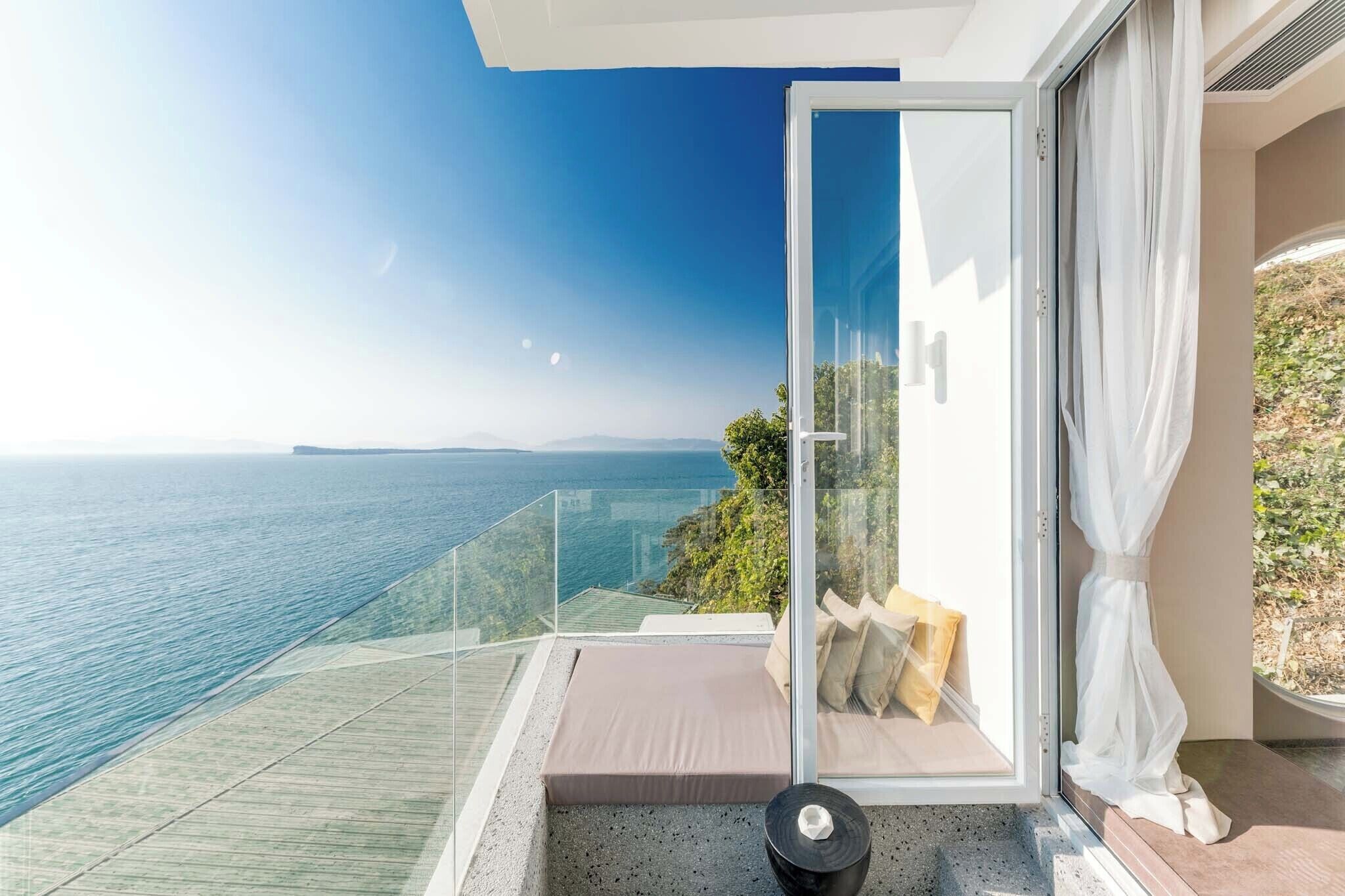 A balcony with a glass railing overlooking a body of water and distant land.