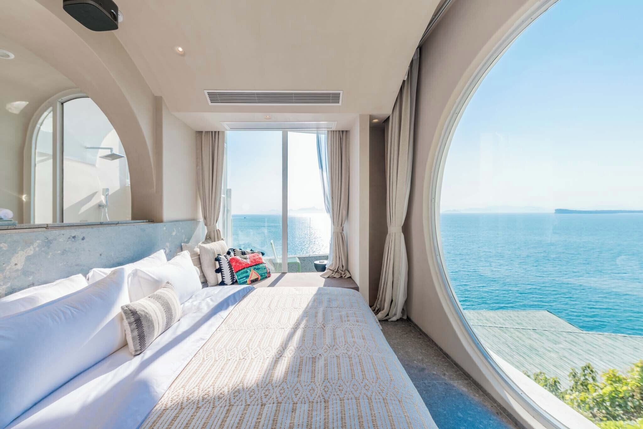 A bedroom with a large bed, a window with a view of the sea, and a ceiling fan.