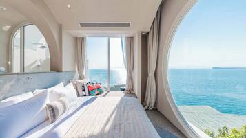 A bedroom with a large bed, a window with a view of the sea, and a ceiling fan.