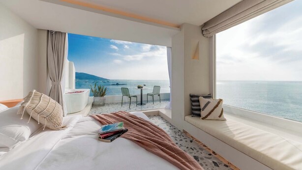 Une chambre avec une grande fenêtre donnant sur une piscine et la mer.