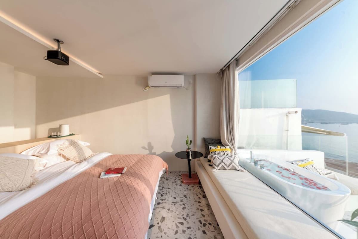 Une chambre d’hôtel avec deux lits, une petite table, une plante et un balcon donnant sur la mer.