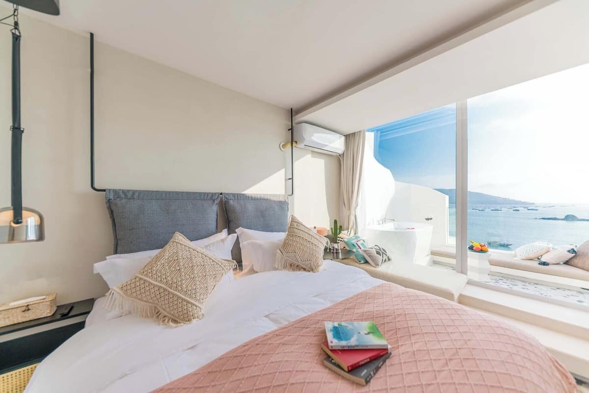 Une chambre d’hôtel avec un grand lit, une table de chevet, une lampe et une vue sur la mer.