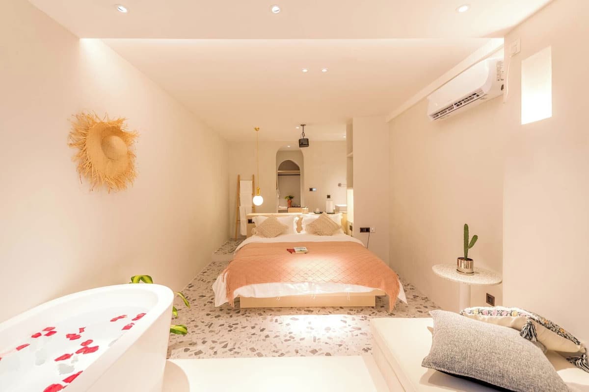 Une chambre moderne avec un grand lit, une baignoire remplie de pétales de roses, un petit cactus et un miroir.