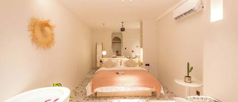 Ein modernes Schlafzimmer mit einem großen Bett, einer Badewanne voller Rosenblätter, einem kleinen Kaktus und einem Spiegel.